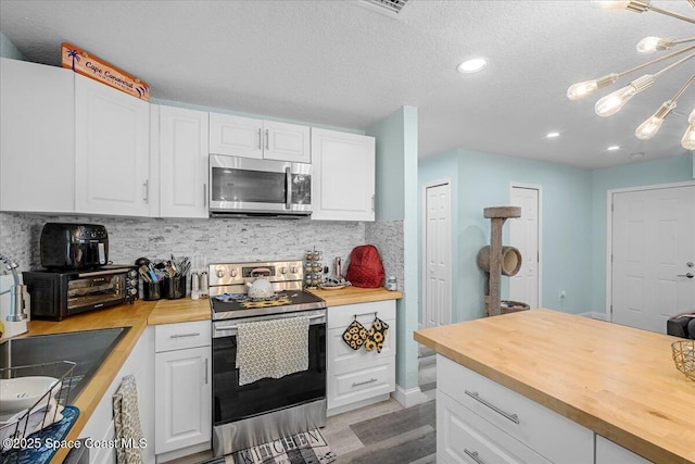 kitchen featuring decorative backsplash, white cabinetry, wooden counters, and stainless steel appliances