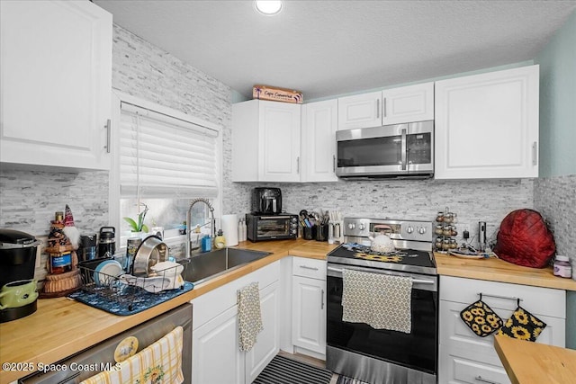 kitchen featuring wooden counters, a sink, stainless steel appliances, white cabinetry, and backsplash