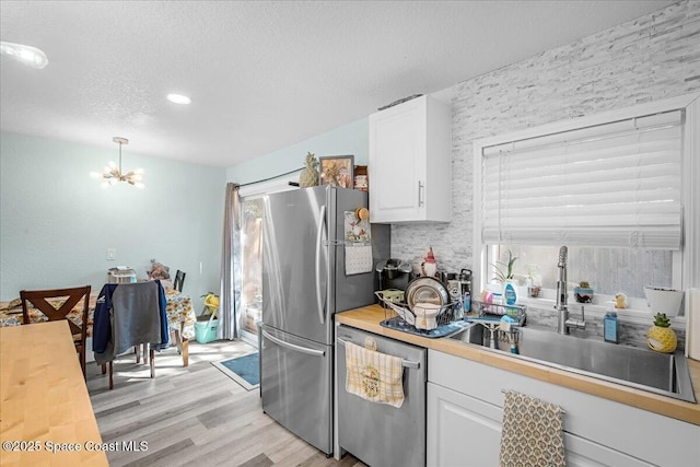 kitchen with a sink, appliances with stainless steel finishes, a chandelier, and white cabinetry