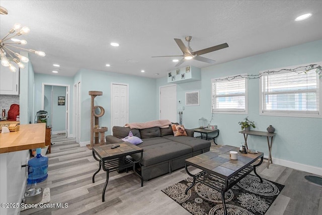 living area featuring a ceiling fan, baseboards, visible vents, light wood-style floors, and a textured ceiling