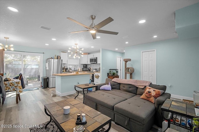 living room with light wood-style flooring, recessed lighting, ceiling fan with notable chandelier, and visible vents