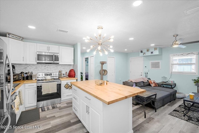 kitchen featuring butcher block countertops, open floor plan, appliances with stainless steel finishes, white cabinetry, and tasteful backsplash