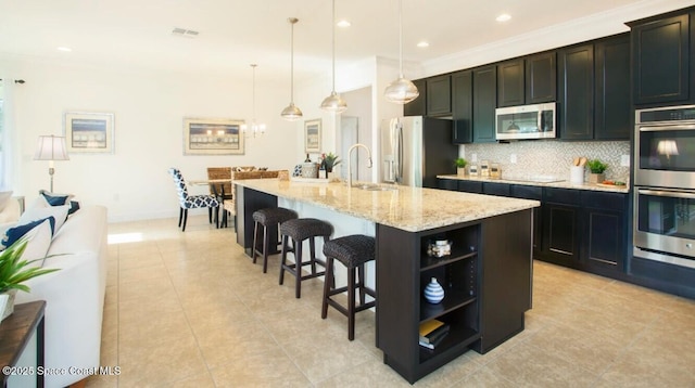 kitchen featuring a breakfast bar, open shelves, backsplash, appliances with stainless steel finishes, and a kitchen island with sink