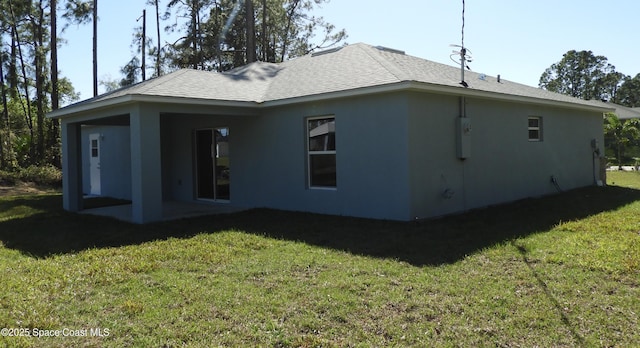 back of property with stucco siding, roof with shingles, and a yard