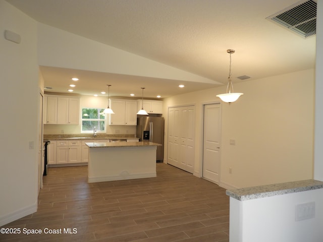 kitchen featuring stainless steel fridge, visible vents, wood tiled floor, vaulted ceiling, and white cabinetry