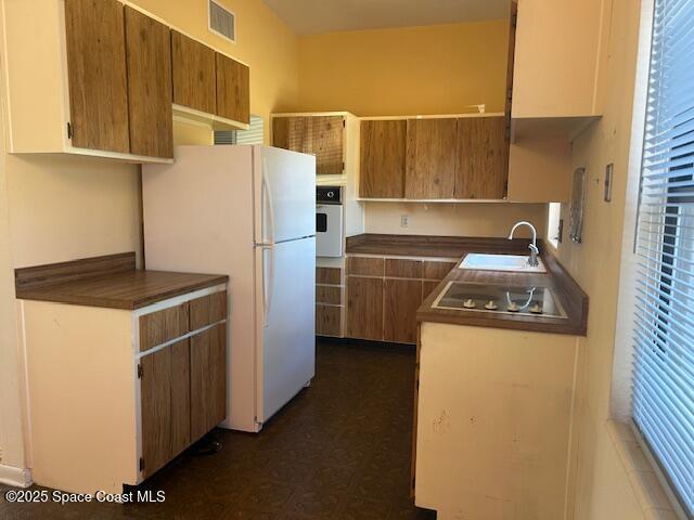 kitchen featuring white appliances, visible vents, a sink, dark countertops, and dark floors