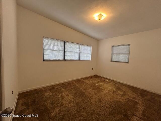 carpeted spare room featuring baseboards and lofted ceiling