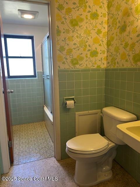 full bath with speckled floor, wallpapered walls, wainscoting, tile walls, and toilet