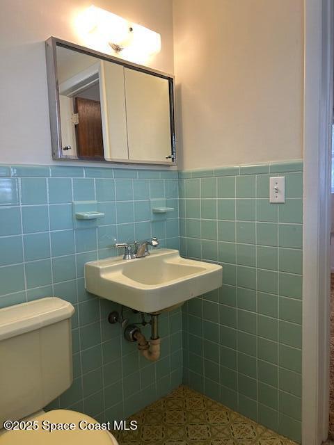 half bath with wainscoting, toilet, tile walls, and a sink