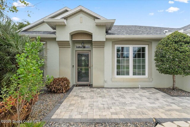 entrance to property with a shingled roof and stucco siding