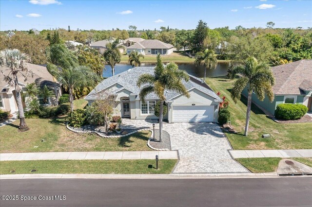 view of front of property featuring an attached garage, decorative driveway, a front yard, and a water view