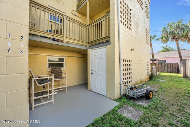 exterior space with concrete block siding, a balcony, and fence