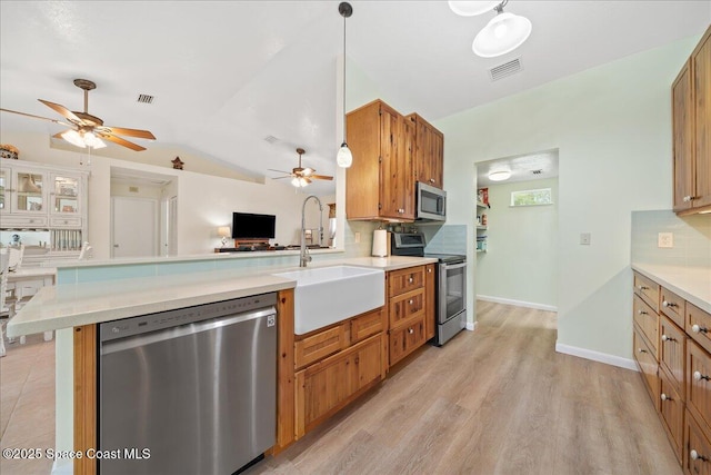 kitchen featuring backsplash, appliances with stainless steel finishes, brown cabinetry, a sink, and a peninsula