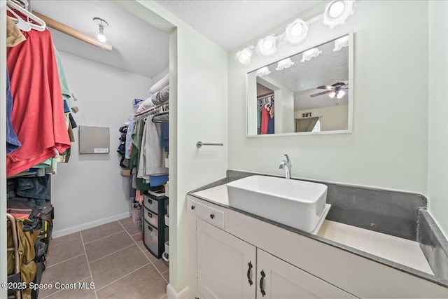 bathroom with a ceiling fan, tile patterned flooring, a walk in closet, a textured ceiling, and vanity