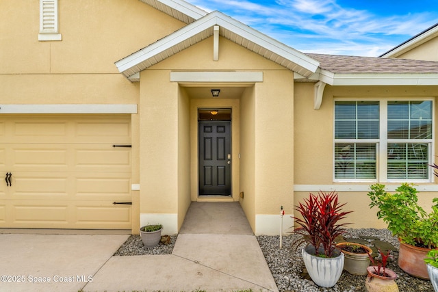 property entrance featuring a shingled roof, an attached garage, and stucco siding