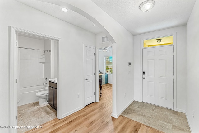 entrance foyer with light wood finished floors, visible vents, arched walkways, baseboards, and a textured ceiling