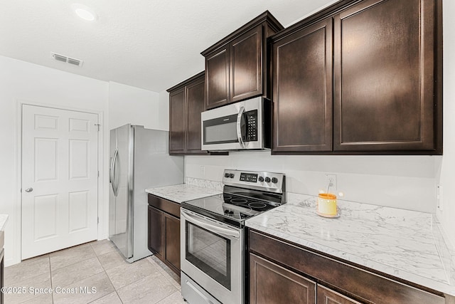 kitchen with light tile patterned floors, a textured ceiling, dark brown cabinetry, visible vents, and appliances with stainless steel finishes