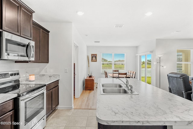 kitchen with stainless steel appliances, visible vents, dark brown cabinetry, a sink, and an island with sink