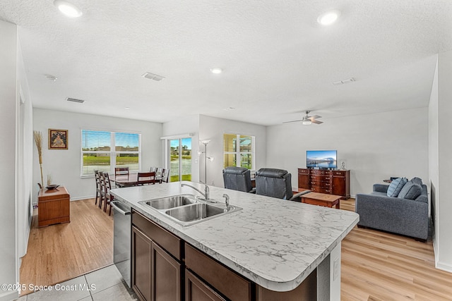 kitchen with light wood finished floors, open floor plan, a sink, an island with sink, and dishwasher