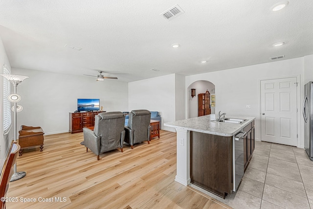 kitchen with arched walkways, a center island with sink, a sink, and visible vents