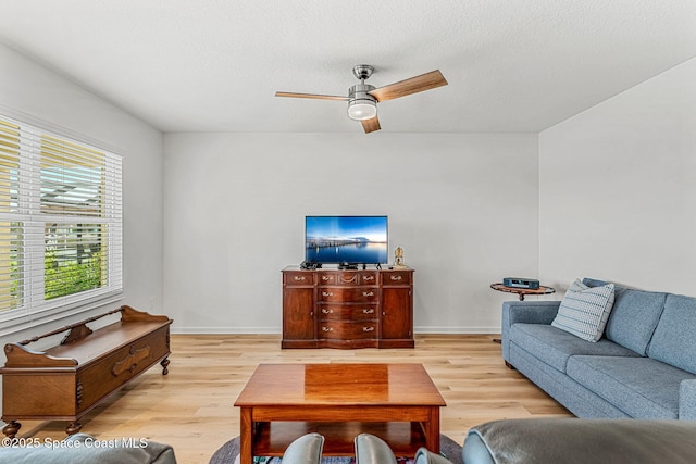 living room featuring a ceiling fan, baseboards, a textured ceiling, and light wood finished floors