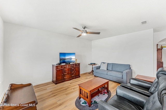 living area featuring arched walkways, ceiling fan, light wood-style flooring, visible vents, and baseboards