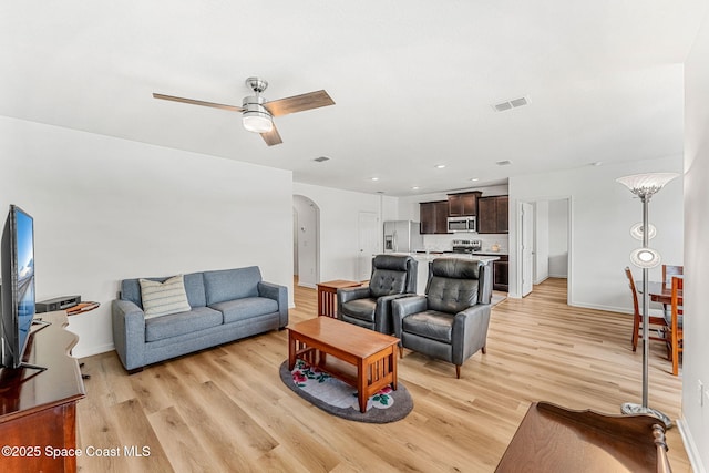 living room with light wood-style flooring, visible vents, arched walkways, and a ceiling fan