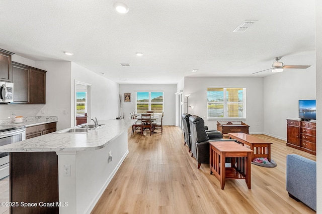 kitchen with appliances with stainless steel finishes, open floor plan, light countertops, dark brown cabinets, and a sink