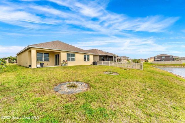 rear view of property with central AC unit, a lawn, fence, and stucco siding