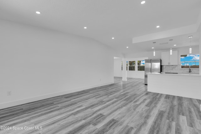 unfurnished living room with light wood-style flooring, recessed lighting, a sink, baseboards, and vaulted ceiling