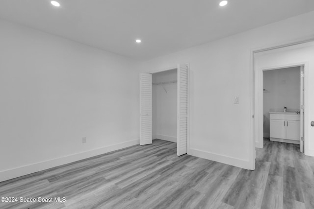 unfurnished bedroom with light wood finished floors, a closet, baseboards, a sink, and recessed lighting