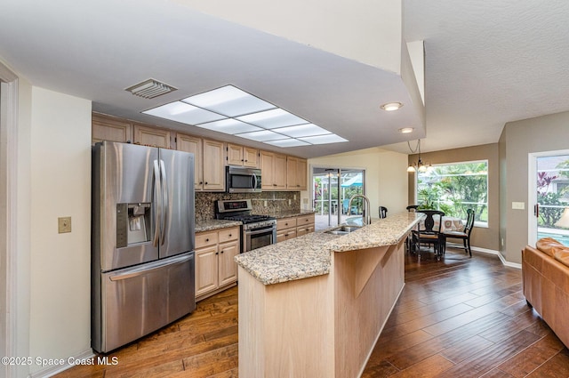 kitchen featuring light stone counters, dark wood finished floors, stainless steel appliances, backsplash, and a sink