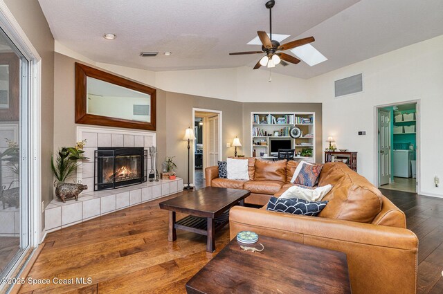 living area with built in shelves, wood-type flooring, a ceiling fan, lofted ceiling with skylight, and a tiled fireplace