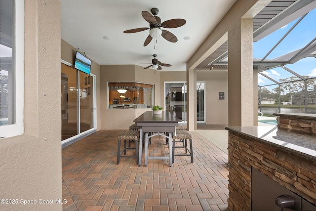 view of patio / terrace featuring glass enclosure, outdoor dining area, and a ceiling fan