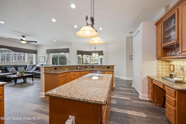 kitchen featuring brown cabinetry, a kitchen island with sink, backsplash, and dark wood-type flooring