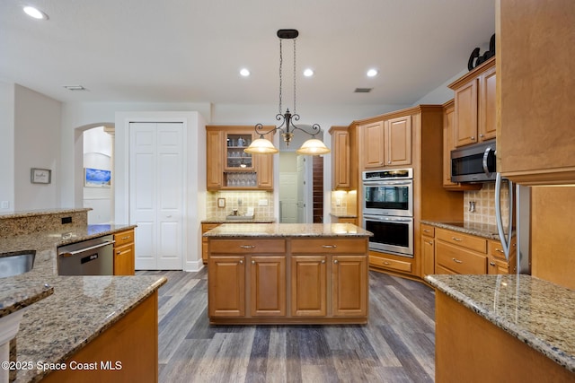 kitchen with arched walkways, stainless steel appliances, dark wood-type flooring, and backsplash