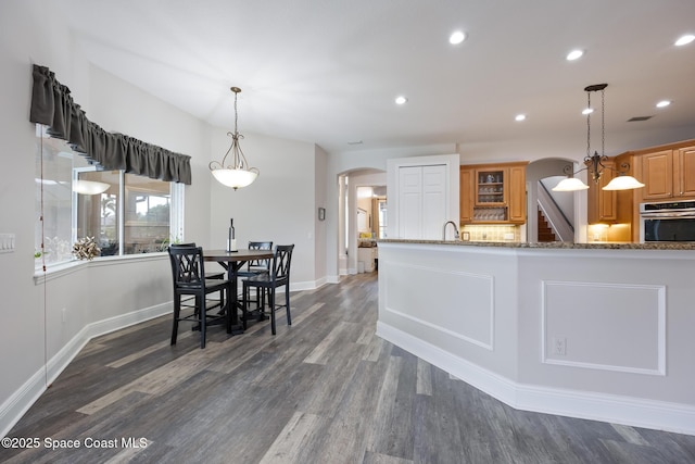 kitchen with arched walkways, dark wood-style flooring, recessed lighting, stainless steel oven, and light stone countertops