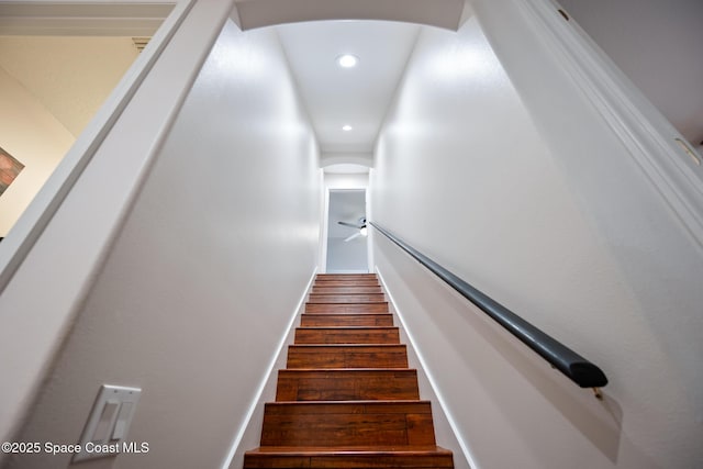 stairway with arched walkways, wood finished floors, and recessed lighting