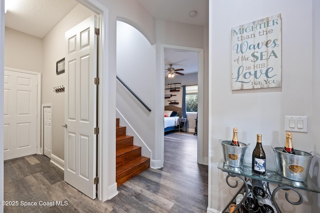 foyer entrance with dark wood-style floors, arched walkways, baseboards, and stairs