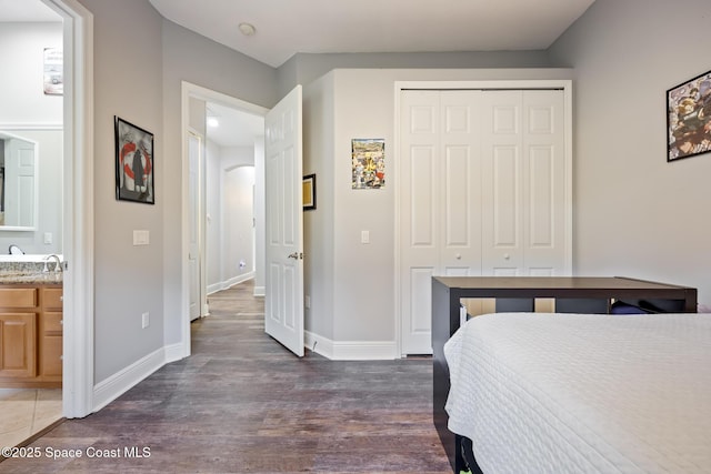 bedroom featuring a closet, ensuite bathroom, baseboards, and wood finished floors