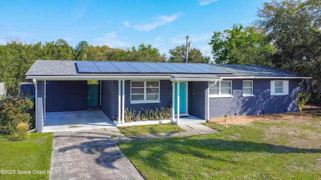 ranch-style home with concrete block siding, solar panels, a carport, driveway, and a front lawn