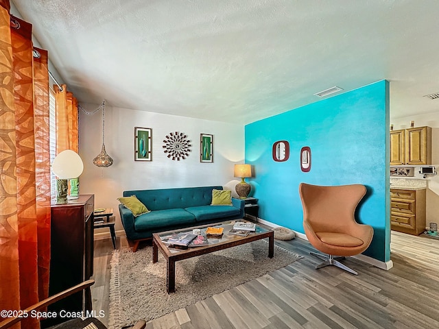 living room with baseboards, visible vents, a textured ceiling, and light wood finished floors