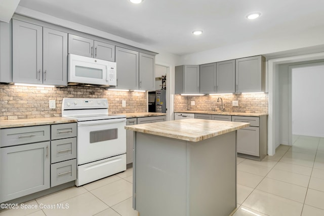 kitchen with light tile patterned floors, gray cabinets, a kitchen island, a sink, and white appliances