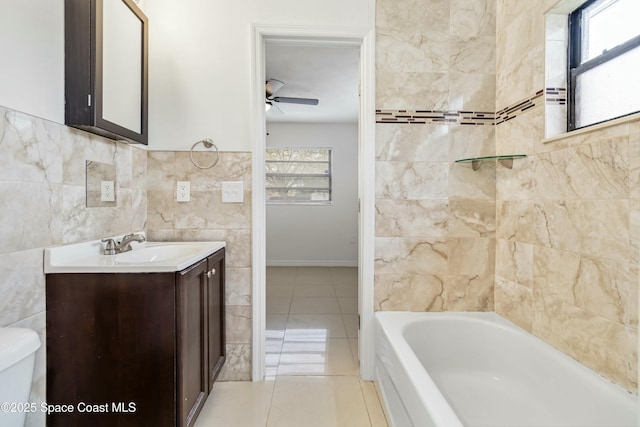 full bath featuring a tub to relax in, toilet, vanity, tile walls, and a ceiling fan