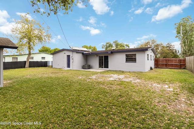 rear view of property with a yard, solar panels, a fenced backyard, and stucco siding