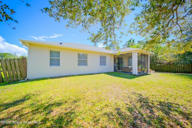 rear view of property featuring a sunroom, fence, stucco siding, and a yard