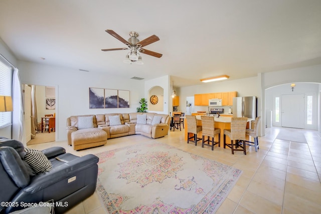 living area with arched walkways, visible vents, ceiling fan, and light tile patterned floors