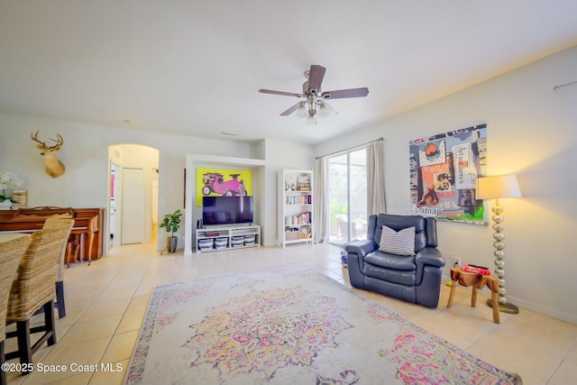 tiled living area featuring arched walkways, ceiling fan, and baseboards