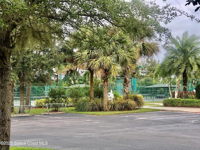 view of home's community with a tennis court, fence, and uncovered parking