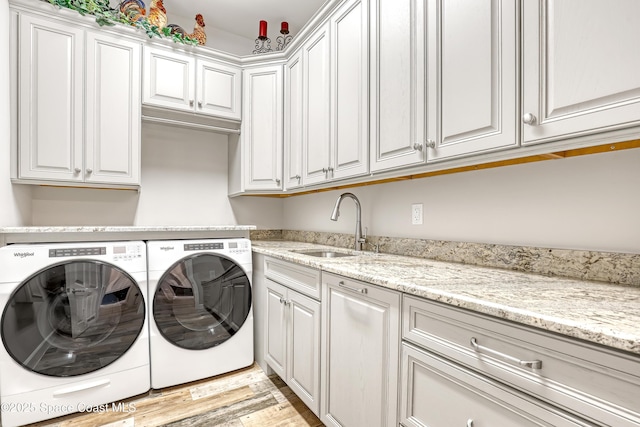 clothes washing area with a sink, cabinet space, light wood-style flooring, and washer and clothes dryer